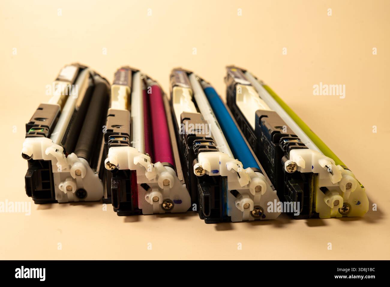 Quatre cartouches d'imprimante couleur disposées en rangée sur un fond beige représentent les fournitures d'impression, la maintenance et le service de bureau Banque D'Images