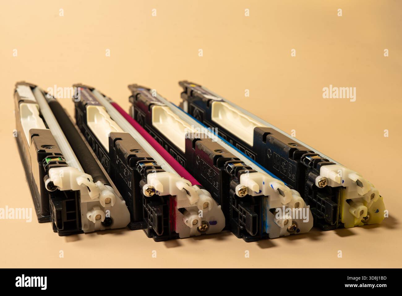 Quatre cartouches d'imprimante couleur disposées en rangée sur un fond beige représentent les fournitures d'impression, la maintenance et le service de bureau Banque D'Images