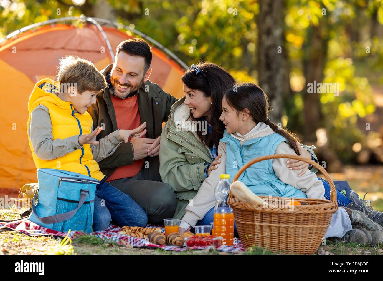Famille avec deux enfants appréciant ensemble pique-niquer dans un parc animé entouré d'arbres et de couleurs d'automne Banque D'Images