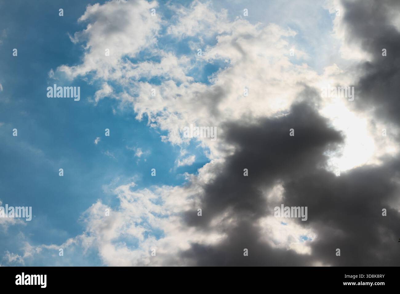 Le soleil caché derrière une masse de nuages gris foncé, avec des rayons de lumière et des ombres sur le ciel bleu, pour le fond Banque D'Images