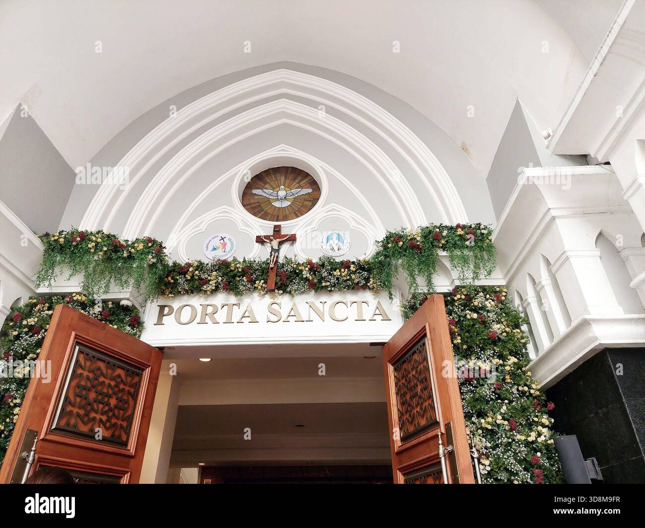 Belle entrée de l'église avec des décorations florales, des portes en bois et une architecture en arc ornée. Idéal pour les thèmes de la religion, cérémonie, architecture, a Banque D'Images