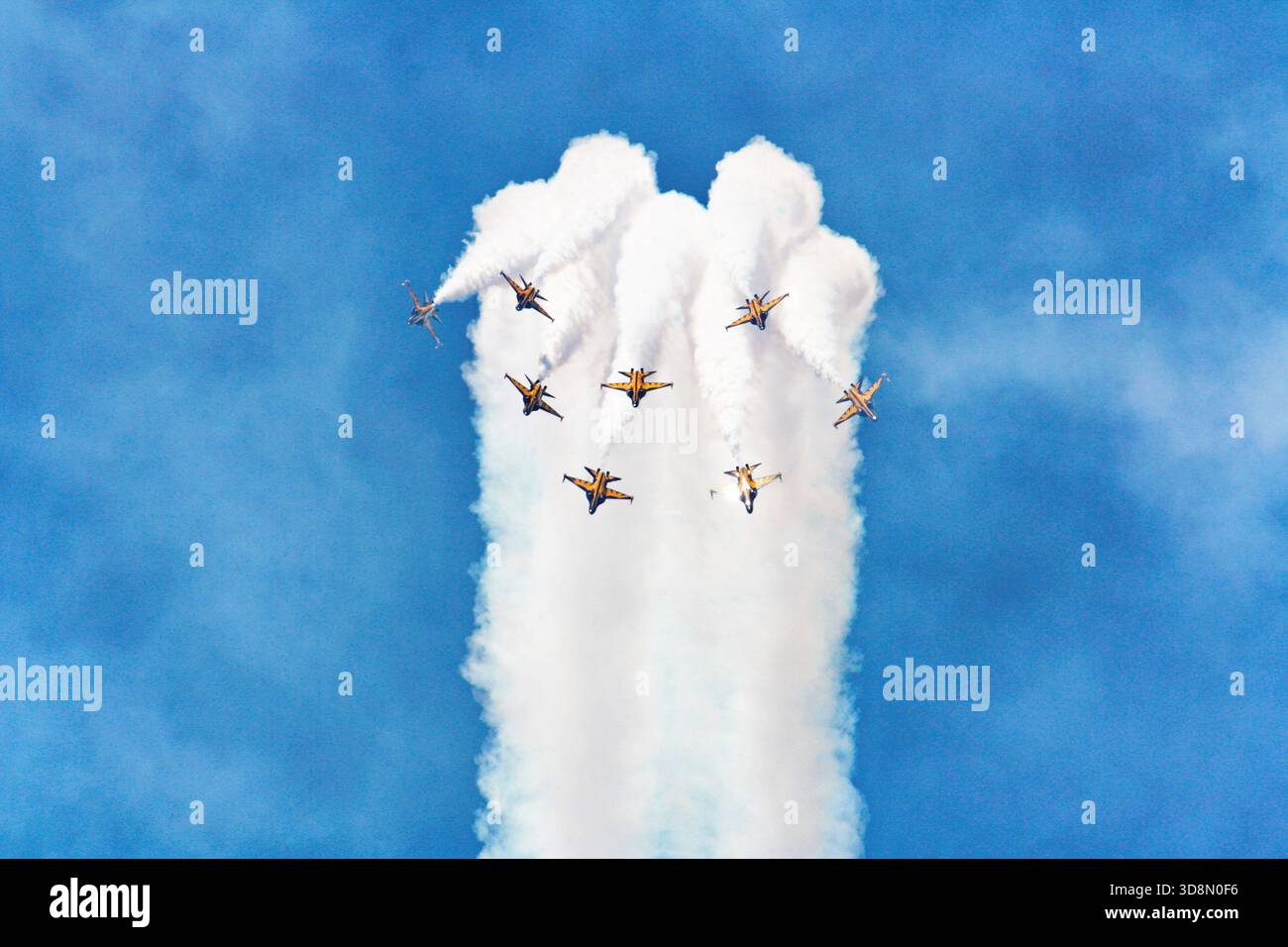 Neuf avions de chasse colorés exécutent une manœuvre aérienne en forme de losange, créant des traînées de fumée blanche ressemblant à des formations à double cône contre un... Banque D'Images