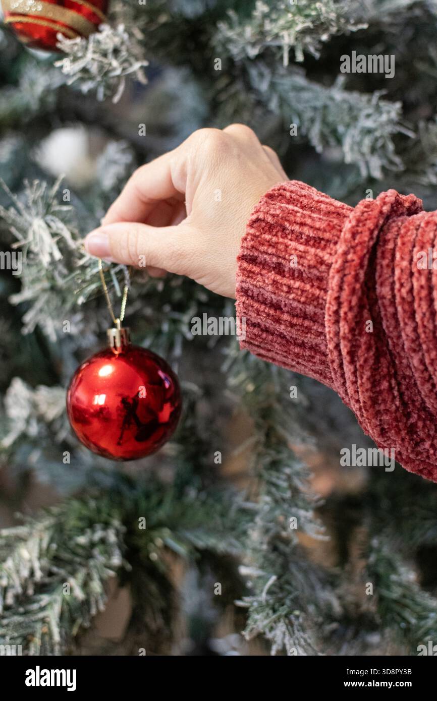 Gros plan de la main d’une femme plaçant un ornement de Noël sur un arbre décoré Banque D'Images