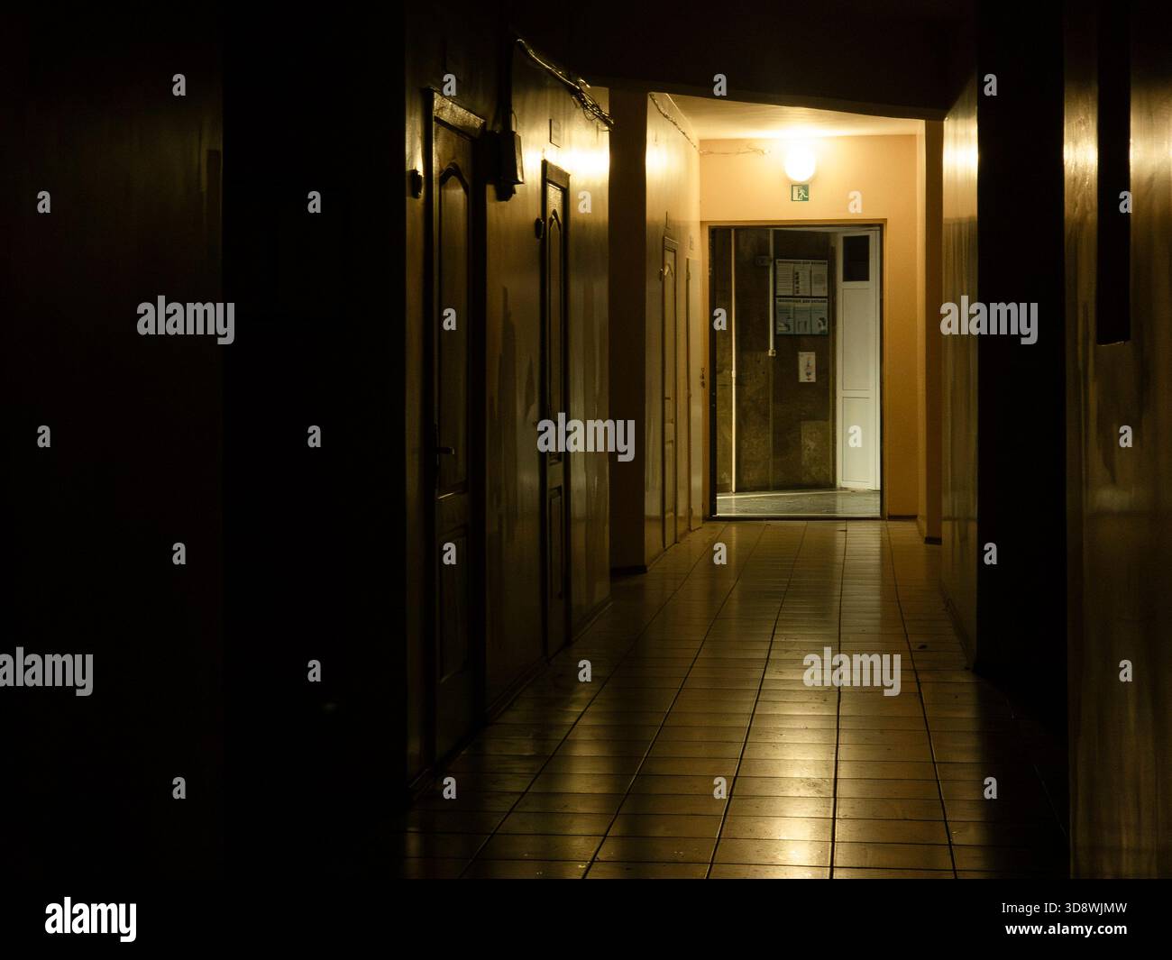 Long couloir étroit créant un sentiment de mystère et de suspense, avec une série de portes fermées sur la gauche et une source lumineuse lointaine éclairant le Banque D'Images