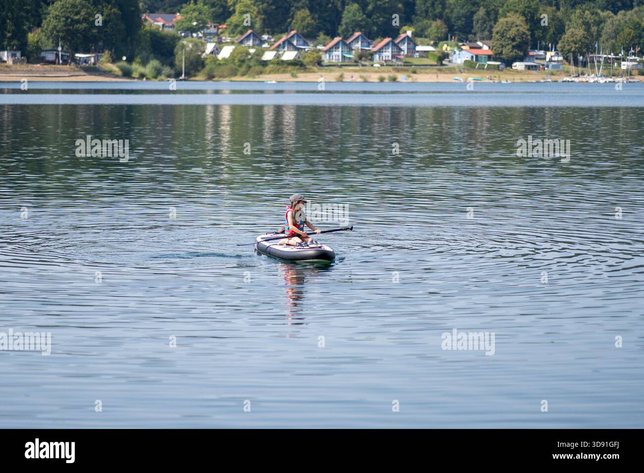 Fille dans l'eau tenant le panneau SUP tandis que l'ami reste sur le dessus, la sécurité de l'eau de l'enfant d'été et le concept de sauvetage au milieu du lac avec l'espace de copie Banque D'Images