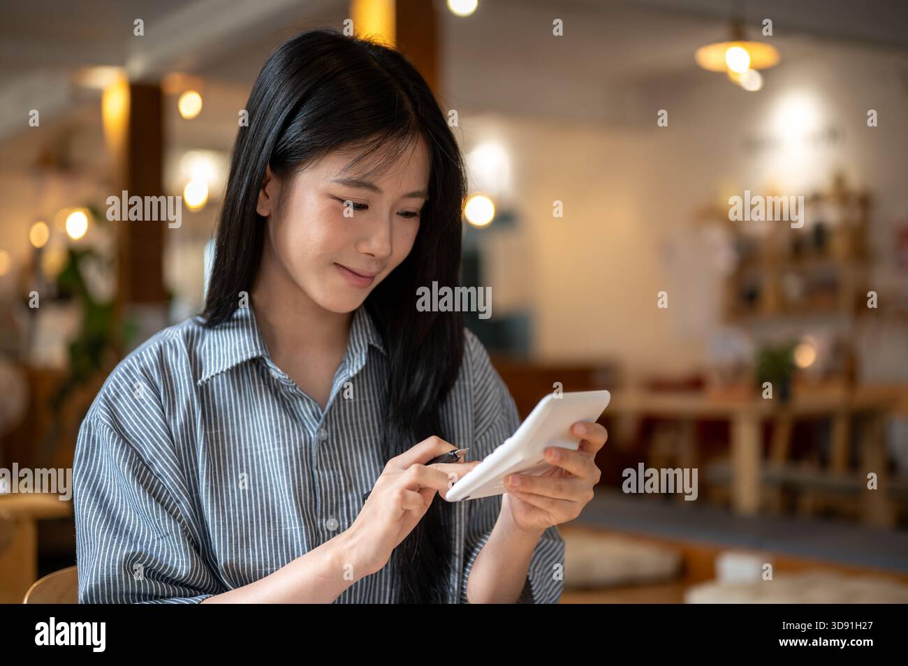 Femme asiatique souriante tenant et utilisant une calculatrice blanche tout en étant assis à la table en bois dans le café. Revenus et dépenses. Gestion de l'argent. Banque D'Images