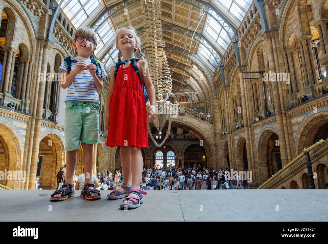 Les enfants avec des sacs à dos explorent le musée sous le squelette géant de baleine Banque D'Images