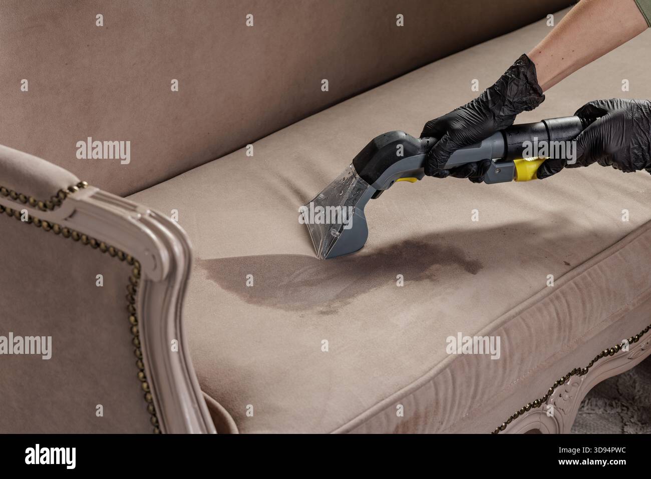 Travailleur ganté utilisant une buse d'aspiration de rembourrage pour enlever la tache de liquide fraîche du coussin de canapé en tissu Banque D'Images