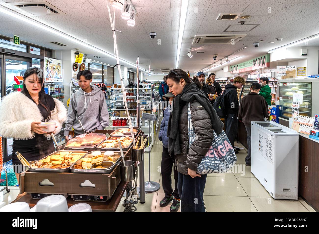Clients au comptoir des aliments chauds dans un dépanneur à Hakone, préfecture de Kanagawa, Japon. La gamme – établie au Japon comme un « fast food » de style japonais – comprend de l’oden (ragoût), du karaage (poulet frit) et des plats similaires ; les clients comprennent des touristes internationaux Banque D'Images
