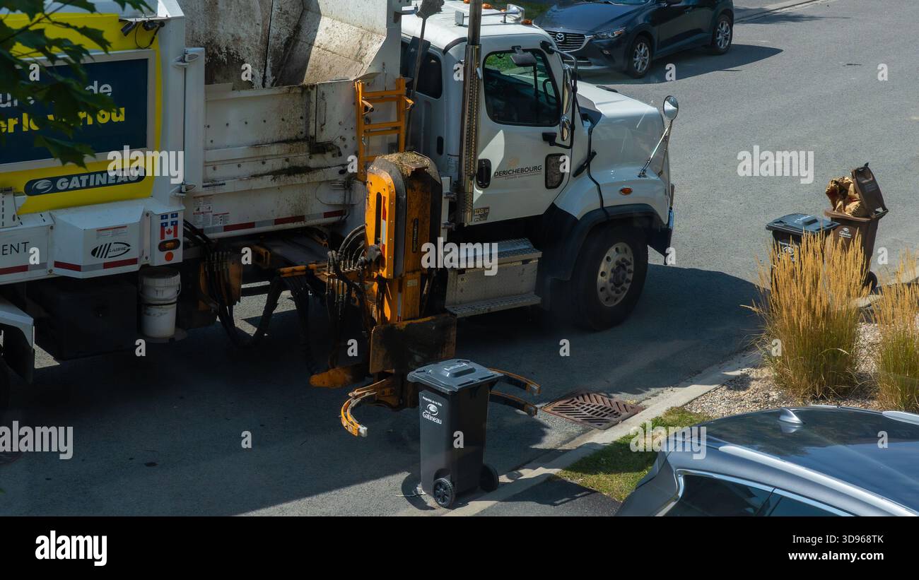 Gatineau QC, Canada - 10 septembre 2025 : camion à ordures ramasse les déchets des poubelles en bordure de trottoir par une journée ensoleillée, mettant l'accent sur l'assainissement urbain et commun Banque D'Images