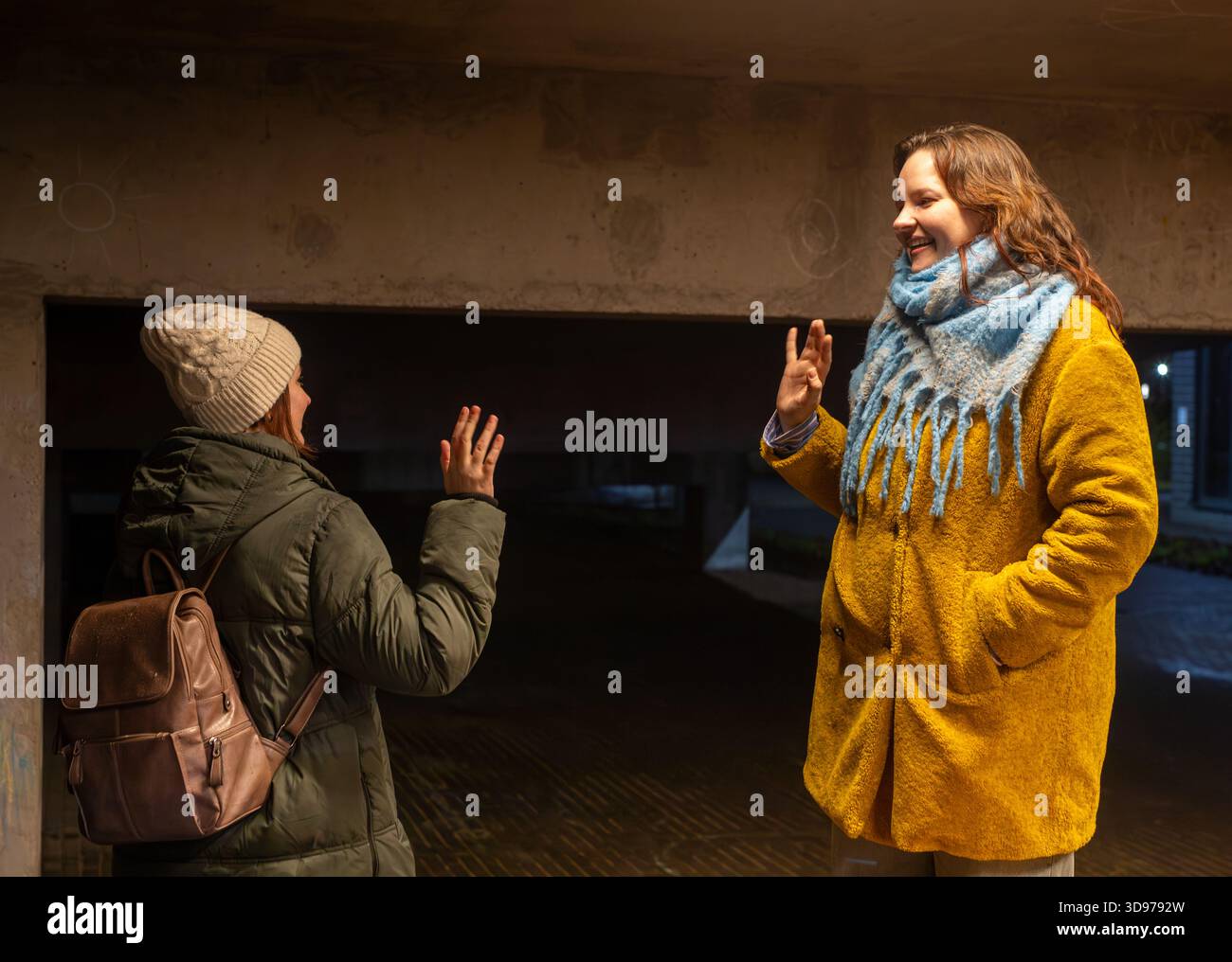 Deux amies se disant au revoir et se faisant signe la nuit, portant des vêtements chauds d'hiver et souriant en se séparant. Banque D'Images