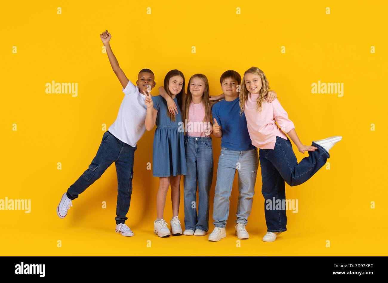 Groupe joyeux d'élèves préadolescents faisant différents gestes sur fond jaune de studio Banque D'Images