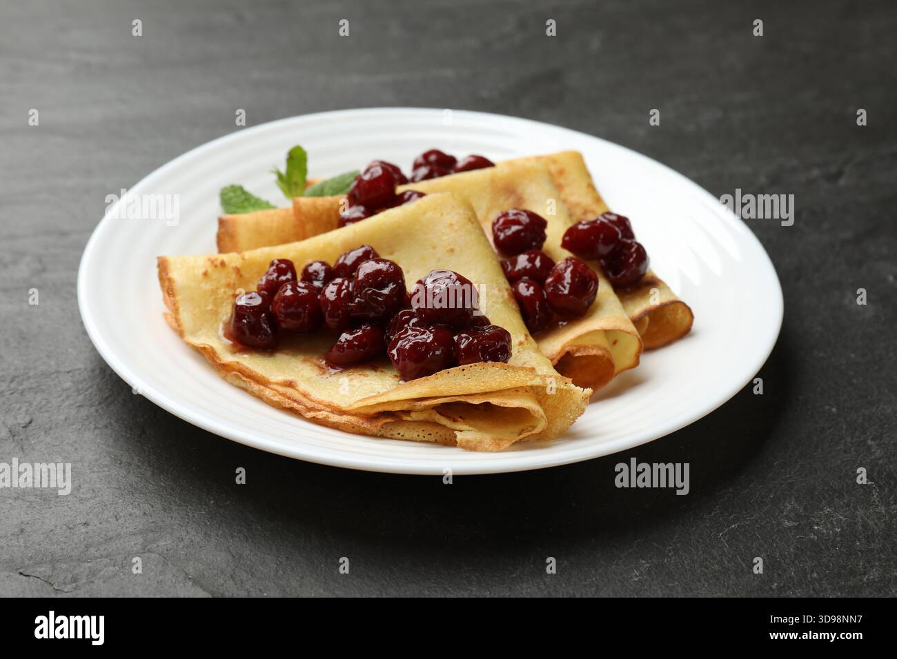 Crêpes savoureuses aux cerises et à la menthe sur table noire, gros plan Banque D'Images