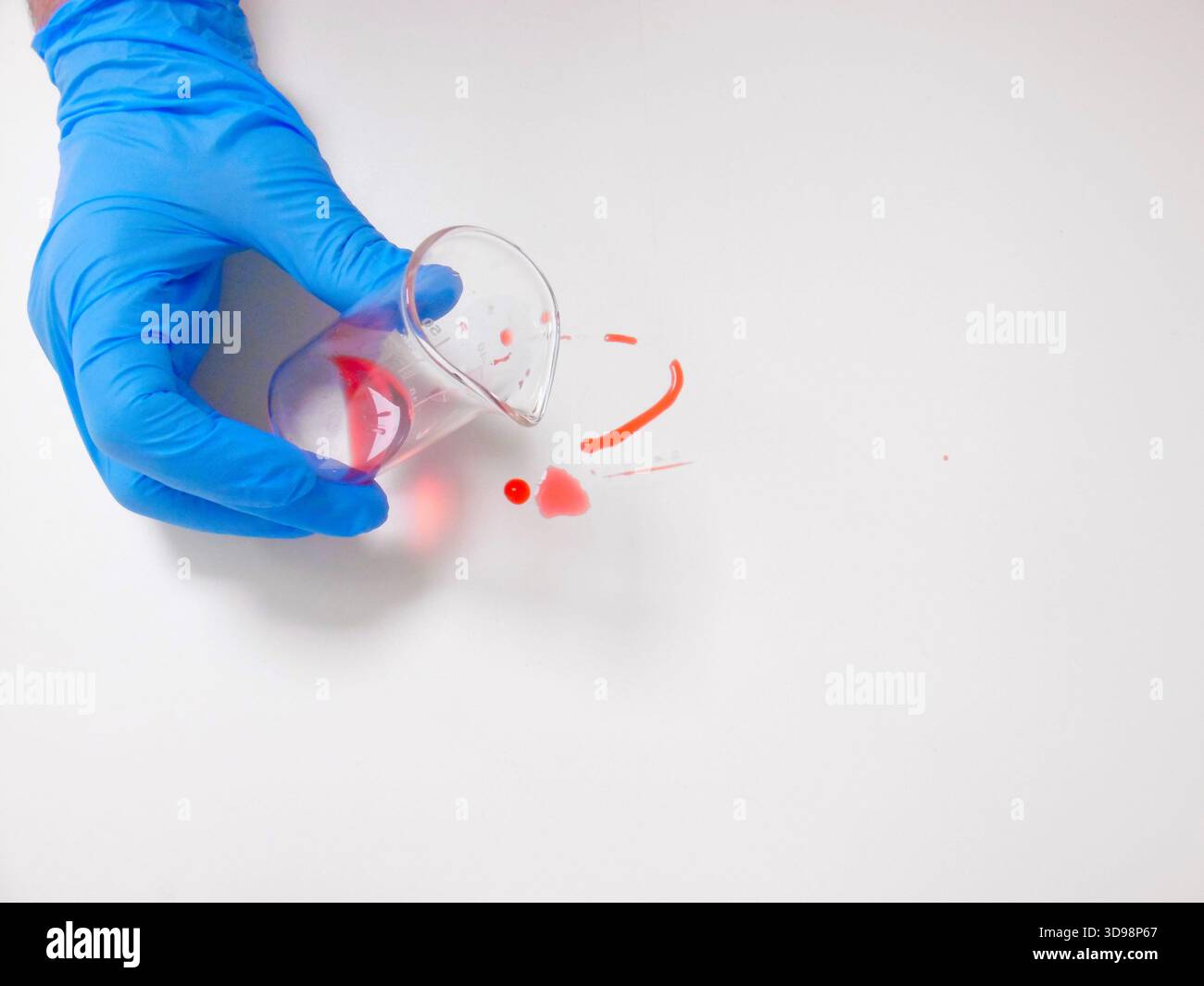 Gobelet inclinable à la main gantée au-dessus d'un frottis rouge sur une surface blanche, démonstration de confinement et de nettoyage Banque D'Images
