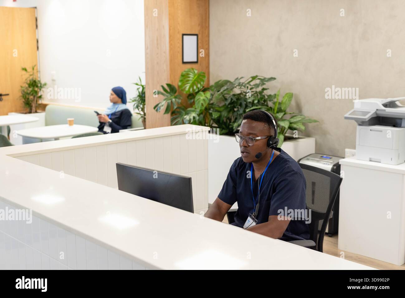 Homme afro-américain au bureau dans les gommages avec casque travaillant sur l'ordinateur tandis que la femme tenant le téléphone Banque D'Images