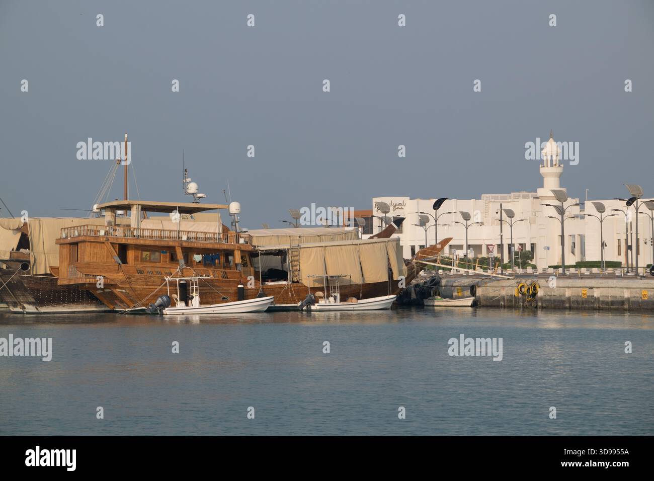Des boutres en bois sont ancrés à la marina de Doha avec des bâtiments modernes visibles sous un ciel dégagé. Banque D'Images