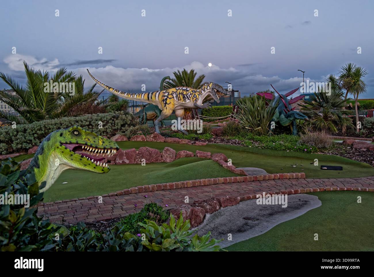 Golf fou avec de grands animaux préhistoriques et palmiers réalistes à la lumière d'une pleine lune à Teignmouth, Devon, Angleterre. Banque D'Images