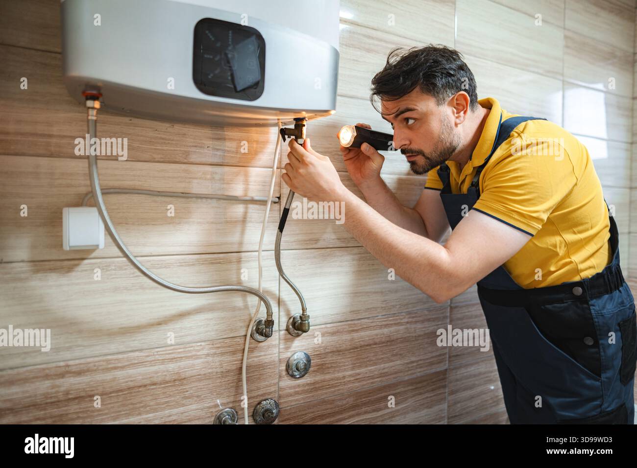 Plombier inspectant chauffe-eau avec lampe de poche dans la salle de bains Banque D'Images
