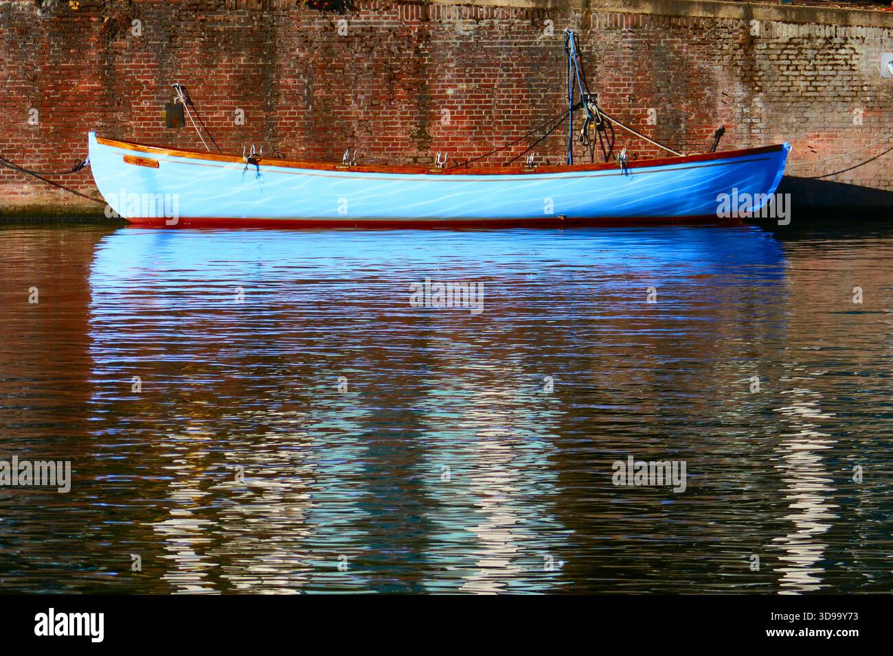Bateau bleu lumineux par mur de briques vieilli avec réflexion de l'eau calme et tranquille canal Vibe à Amsterdam Banque D'Images