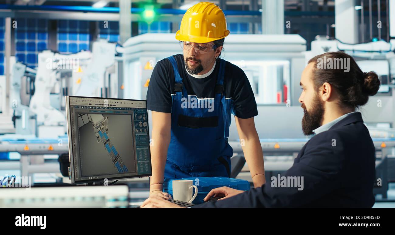 Gestionnaire d'usine photovoltaïque montrant à l'ingénieur sur l'écran du PC comment ajuster les paramètres du système. Spécialiste montrant membre du personnel comment optimiser l'approvisionnement en énergie dans l'usine de fabrication de panneaux solaires, caméra B. Banque D'Images