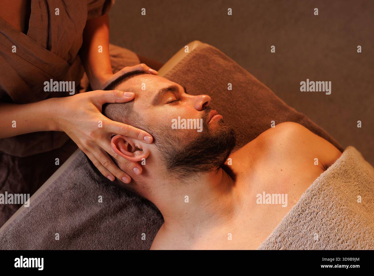 massothérapeute femme faisant massage facial à l'homme, massage d'oreille de près, dans l'atmosphère chaleureuse du salon de massage, concept de massage Banque D'Images