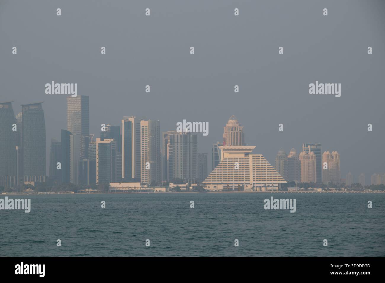 De grands bâtiments bordent le front de mer de Doha sous un ciel brumeux, mettant en valeur l'horizon moderne de la ville près du bord de l'eau. Banque D'Images