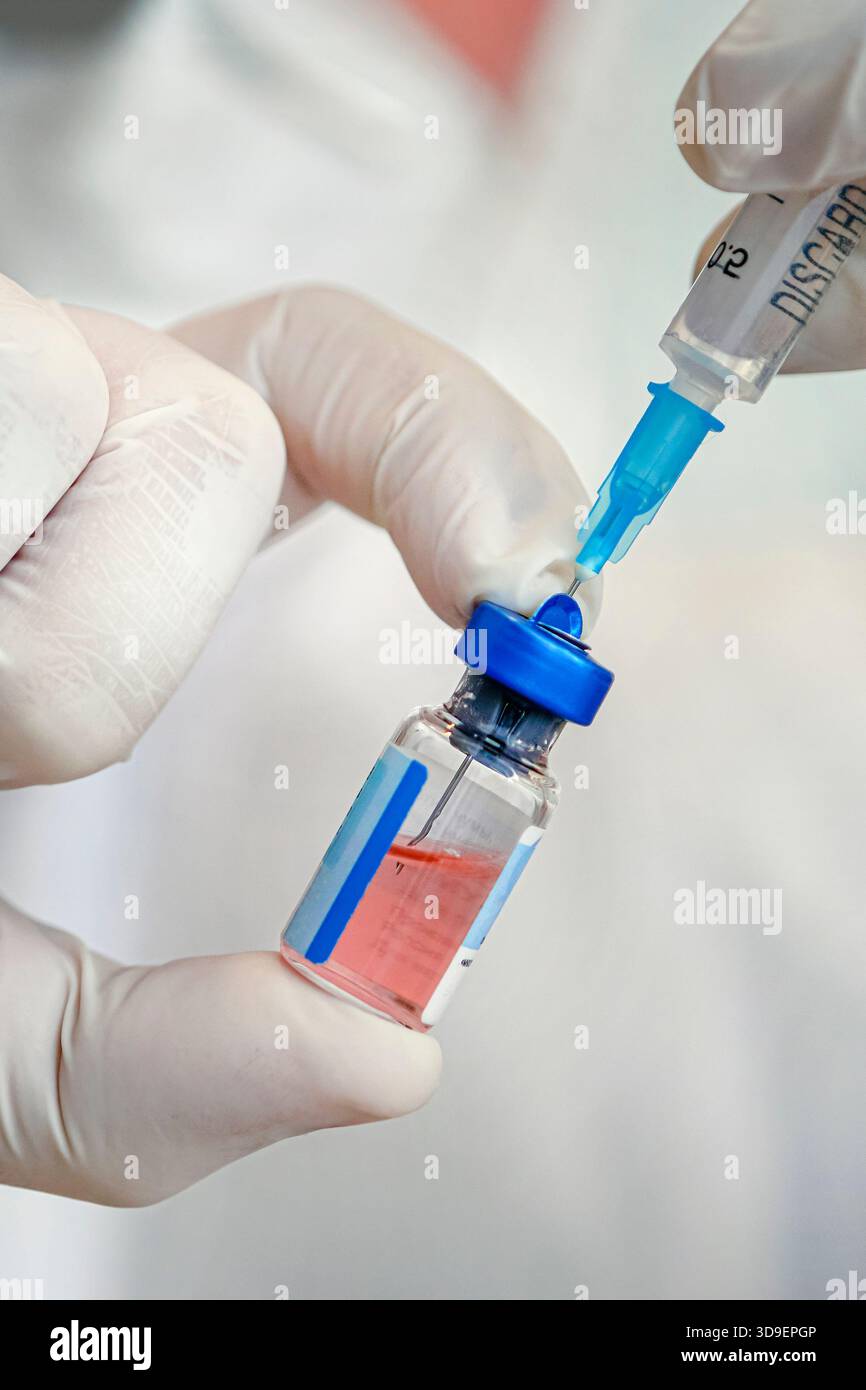 Gros plan d'un scientifique qui interagit avec une seringue et un flacon en verre de vaccin liquide en laboratoire. Banque D'Images