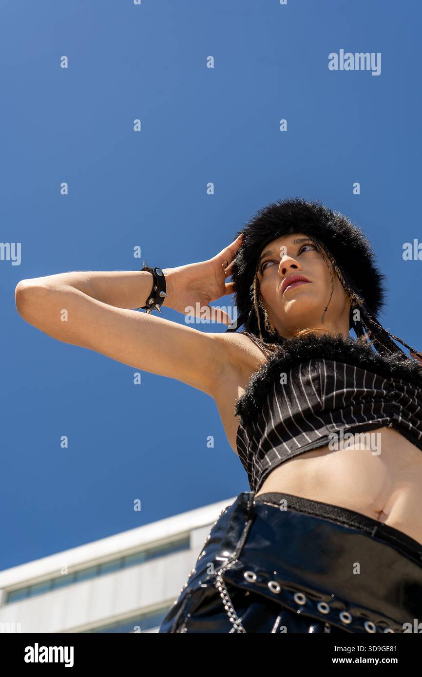 Femme de style alternatif debout à l'extérieur, portant un chapeau en fausse fourrure et un haut à fines rayures, avec un tatouage du ventre unique Banque D'Images
