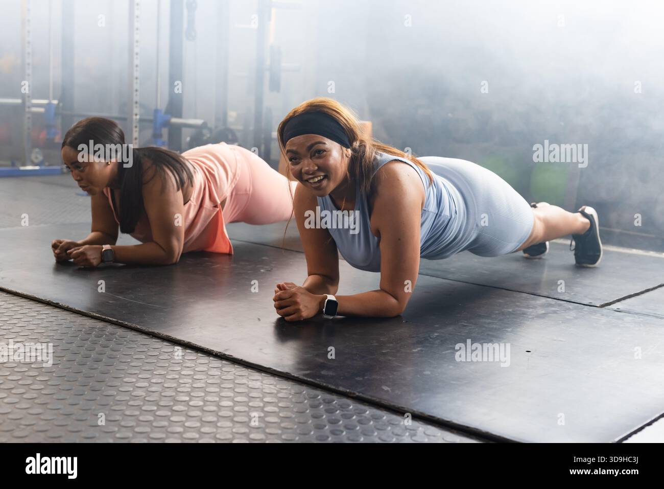 Diverses amies féminines tenant des planches d'avant-bras portant des ensembles de sport à la salle de fitness avec des haltères Banque D'Images