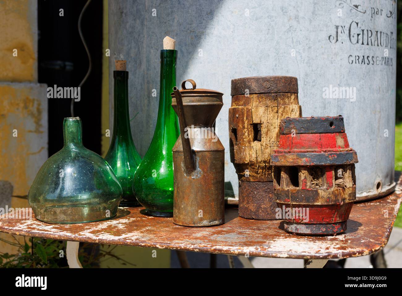 Nature morte vintage avec des bouteilles en verre vert, un grand distributeur d'huile métallique et des outils en bois sur une surface rustique. Lumière naturelle douce, faible profondeur de fie Banque D'Images