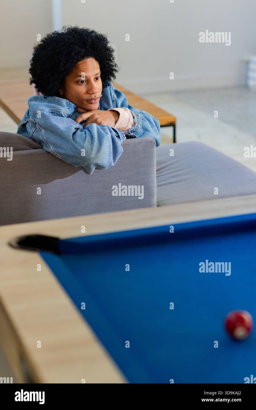 Homme afro-américain appuyé sur un canapé dans le salon de jeux, regardant la table de billard en feutre bleu, espace photocopie Banque D'Images