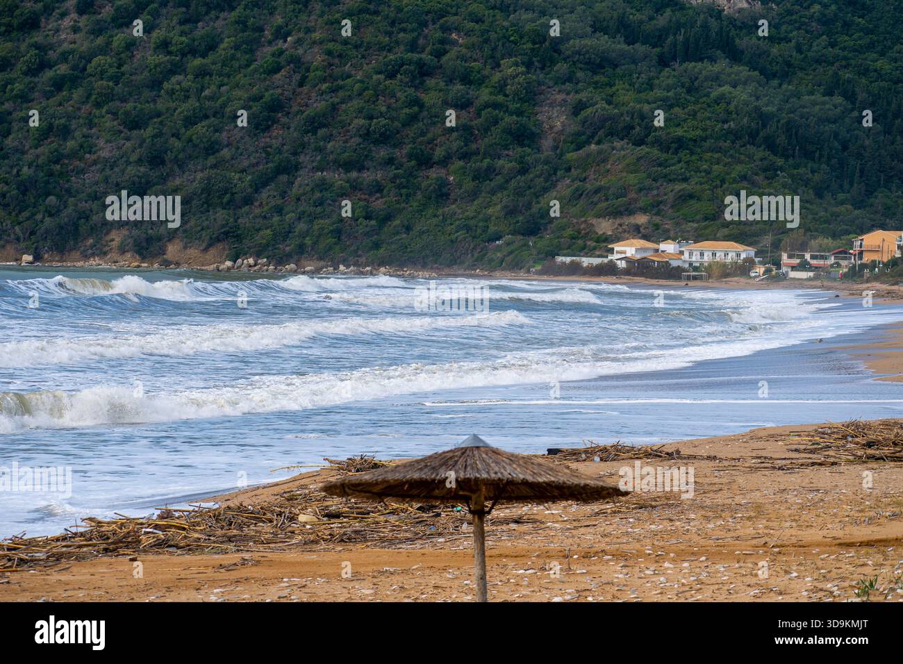 Un parapluie de paille abandonné solitaire se tient sur une plage sale couverte de débris de tempête et de bois flotté avec des vagues blanches rugueuses s'écrasant dans la profondeur de fond Banque D'Images