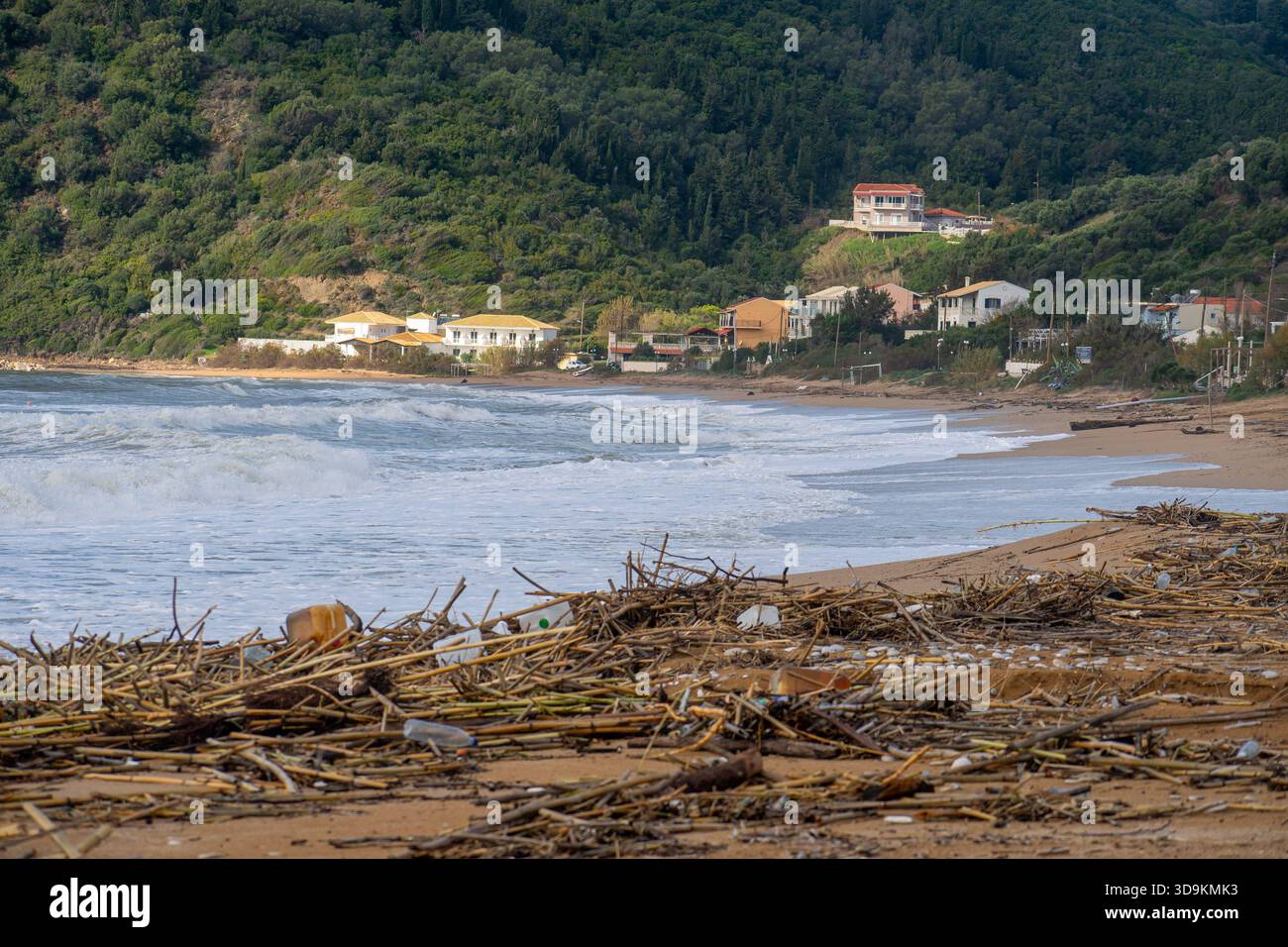 Vagues moussantes blanches rugueuses s'écrasant sur le rivage d'une plage insulaire grecque couverte de bois de dérive lourd et de débris de bambou avec des villas de vacances et des Mo verts Banque D'Images