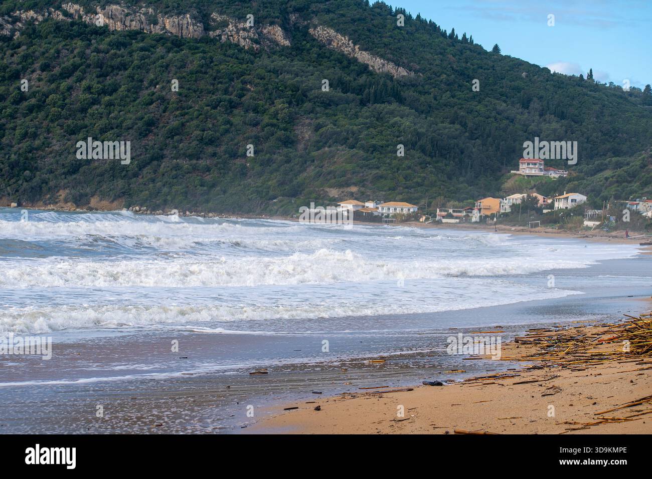 Vaste paysage de vagues moussantes rugueuses lavant sur une plage de sable avec un massif vert montagne en toile de fond et villas côtières à Agios Georgios Corfou Banque D'Images