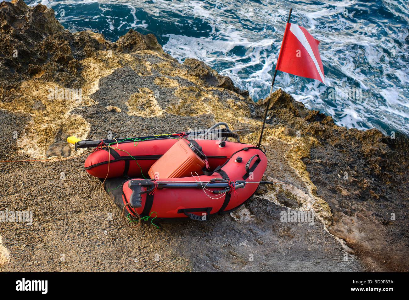 Plongeur rouge flotteur avec un drapeau de sécurité, des pistolets de chasse et des engins de chasse repose sur la rive rocheuse à côté de la mer agitée. Banque D'Images