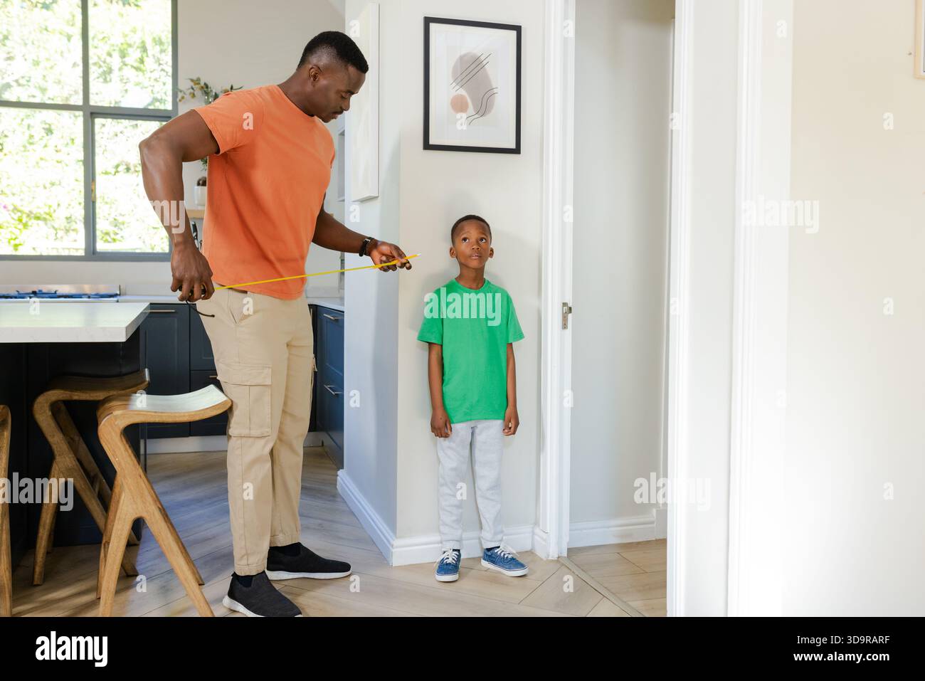 Afro-américain moyen père adulte et enfant mesurant la hauteur à l'aide d'un mètre ruban dans le couloir de la maison Banque D'Images