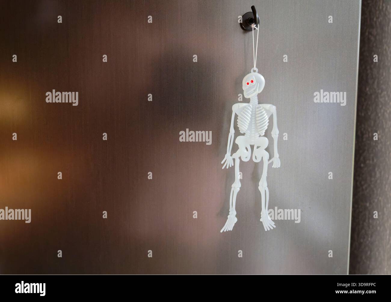 Un petit squelette en plastique aux yeux rouges est accroché à un crochet métallique fixé à une porte ou à un mur, probablement une décoration d'Halloween. Banque D'Images