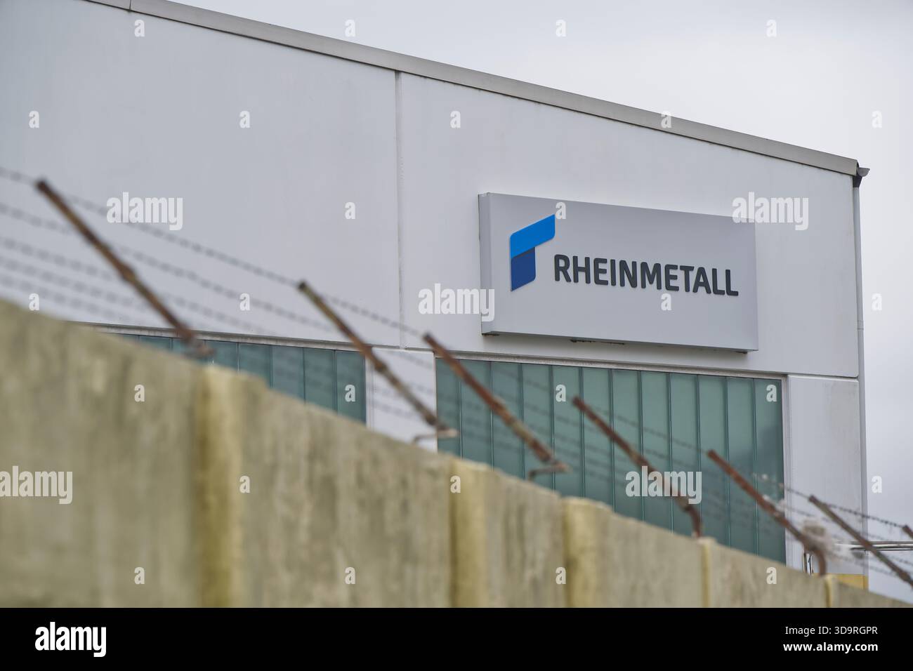 Bâtiment de Rheinmetall avec logo, clôture de fil barbelé au premier plan, ciel couvert. Banque D'Images