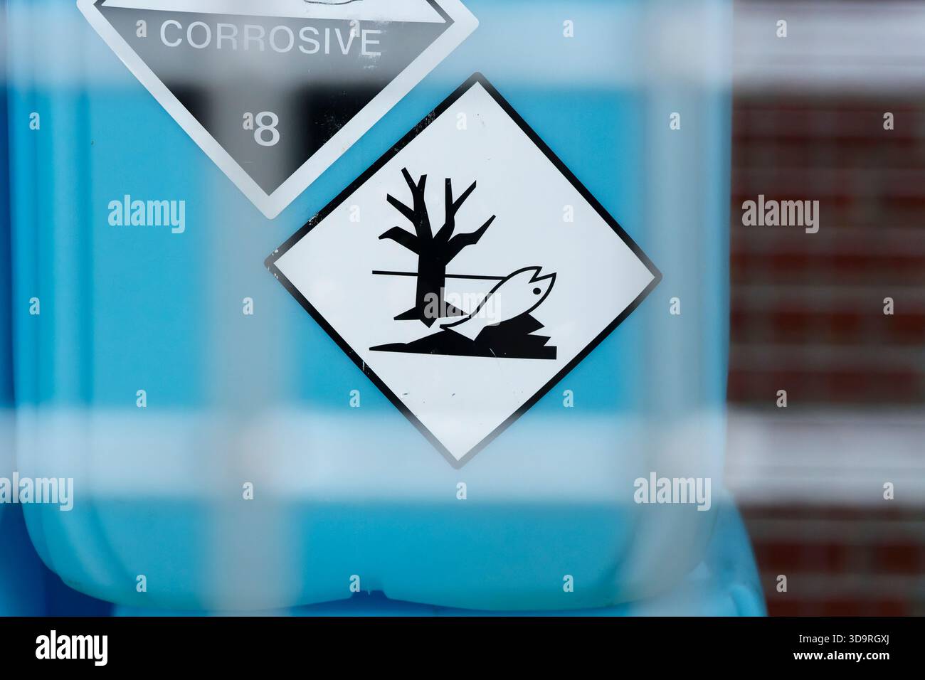 Une étiquette en diamant blanc avec une image noire d'un arbre mort et de poissons est fixée à un grand récipient bleu indiquant les dangers environnementaux et la toxicité pour Banque D'Images