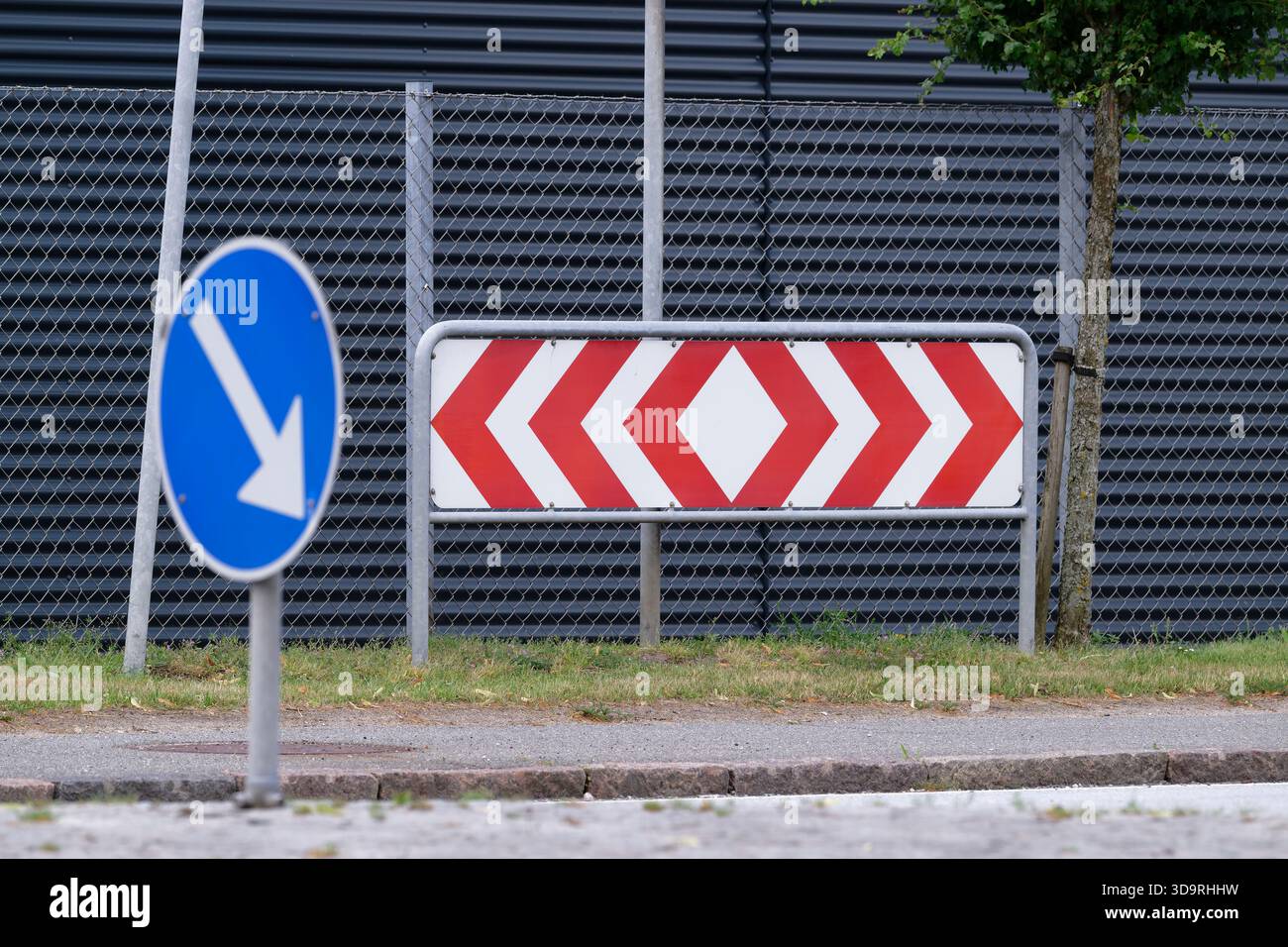 Un panneau de signalisation comportant une série de chevrons rouges indiquant une courbe à l'avant, avec une flèche bleue pointant vers la gauche au premier plan. L'arrière-plan s'affiche Banque D'Images