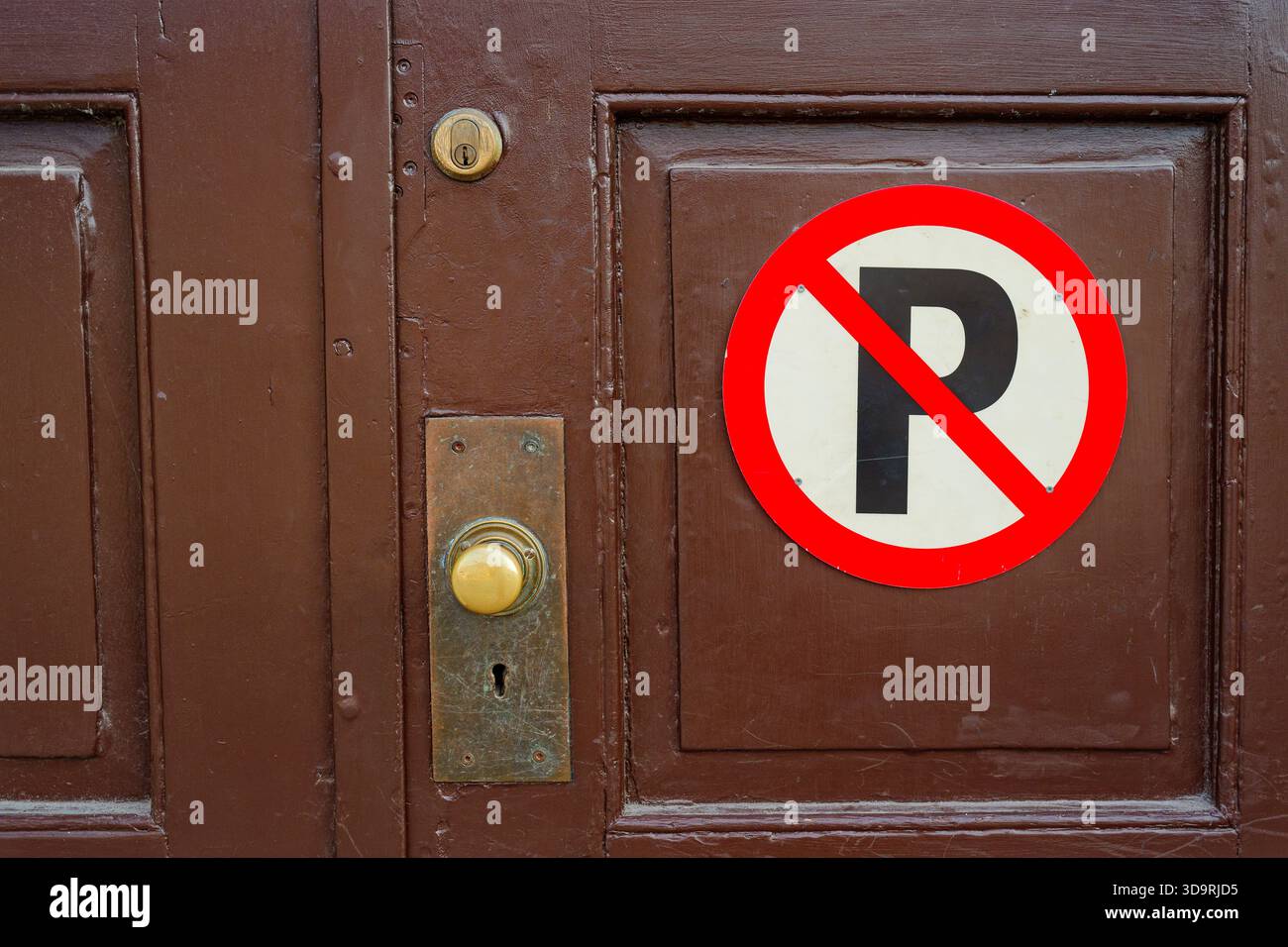 Une porte en bois brun vieilli présente un panneau circulaire rouge avec une lettre P blanche barrée, indiquant qu'il n'y a pas de stationnement. Son placement inhabituel sur une porte i. Banque D'Images