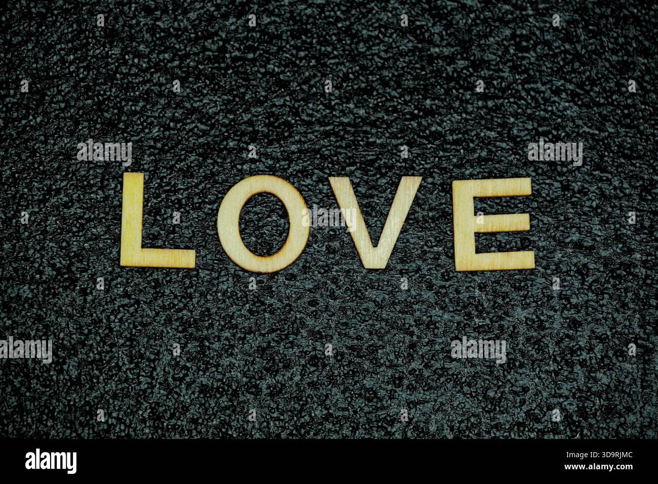 Les lettres en bois disposées pour épeler le mot Love reposent soigneusement sur une surface texturée en caoutchouc noir, créant un contraste visuel simple et frappant. Banque D'Images