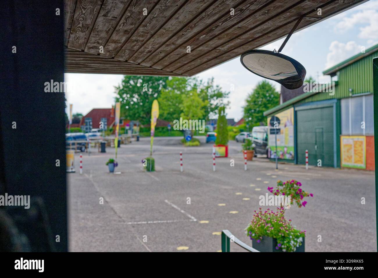 Un petit miroir rond avec un cadre noir est monté sur un long support métallique attaché à un toit en bois au-dessus d'un espace extérieur près des planteurs de poteaux d'asphalte Banque D'Images