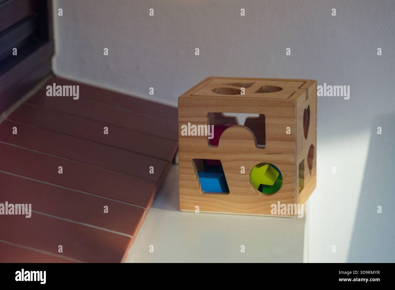 Sur le rebord de la fenêtre repose un cube trieur de forme en bois. De petites pièces solides attendent à l'intérieur, et les fentes correspondantes de chaque côté invitent à jouer, cercle carré triangl Banque D'Images