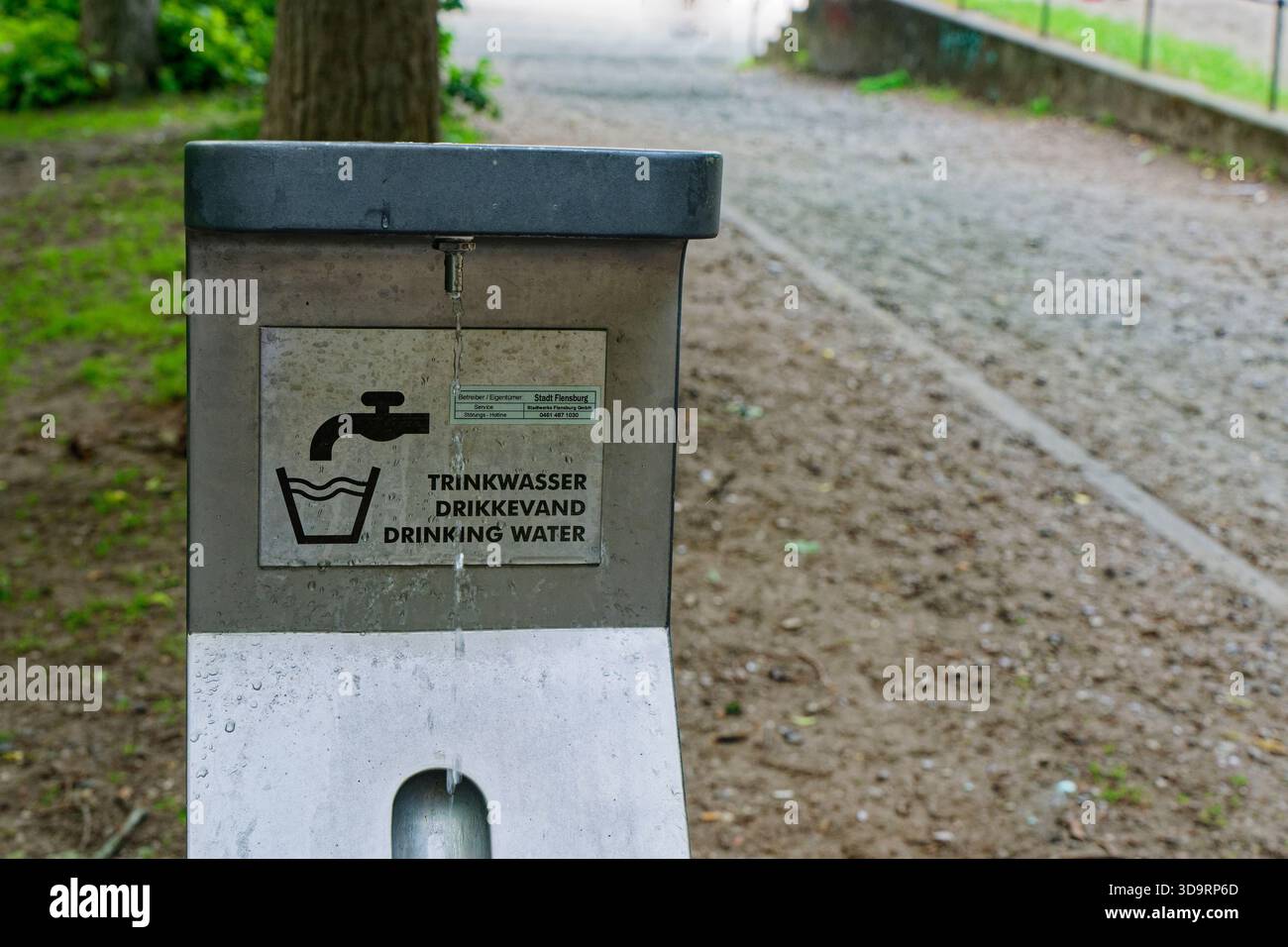 Un bec en métal verse de l'eau fraîche dans un drain, marqué d'un simple trinkwasser et d'un panneau d'eau potable. Service public propre pour la santé, service municipal, Banque D'Images