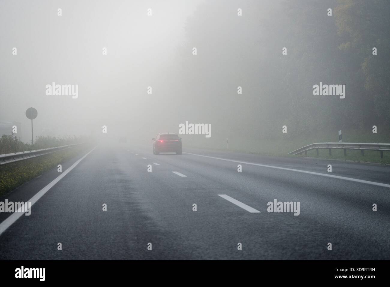 Une voiture isolée glisse vers l'avant sur l'asphalte humide dans un épais brouillard, les lignes s'estompent devant et l'air calme demande patience et rythme prudent pendant que la route s'effondre Banque D'Images