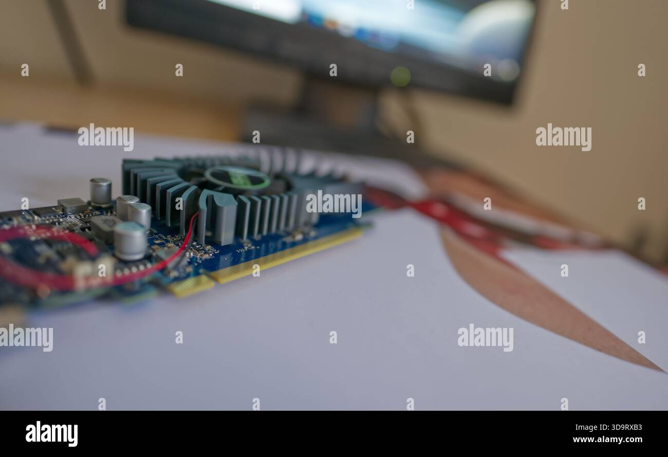 Gros plan d'une carte graphique placée sur une feuille imprimée, avec un écran flou en arrière-plan. L'image met en valeur les détails complexes Banque D'Images