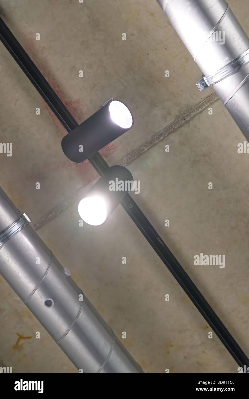 Deux plafonniers modernes montés sur un plafond en béton avec des tuyaux métalliques apparents. Banque D'Images