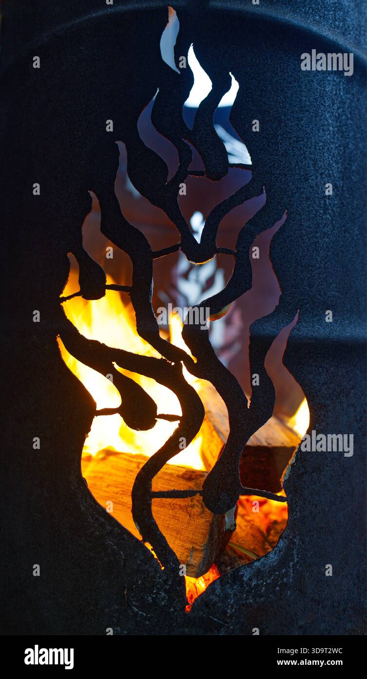 Un foyer décoratif en métal dans un tonneau de feu avec des découpes en forme de flamme, mettant en valeur un feu chaud à l'intérieur. Banque D'Images
