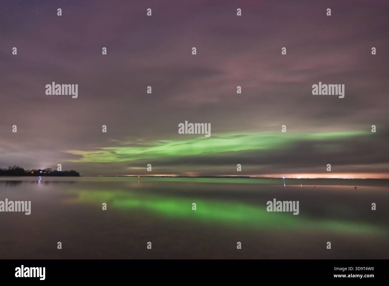 Une scène nocturne sereine avec les aurores boréales se reflétant sur un lac calme sous un ciel nuageux. Banque D'Images